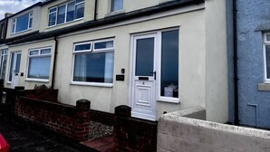 A row of terraced houses with white doors and windows, a brick wall, and a red car parked in front. - Bay View (Morpeth)