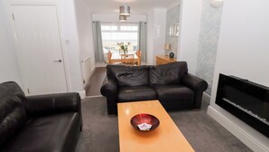 A living room with a black leather sofa, a wooden coffee table, and a flat-screen TV. - Bay View (Morpeth)