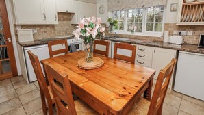 Une cuisine avec une table et des chaises en bois, un vase rempli de fleurs et une fenêtre donnant sur des arbres.