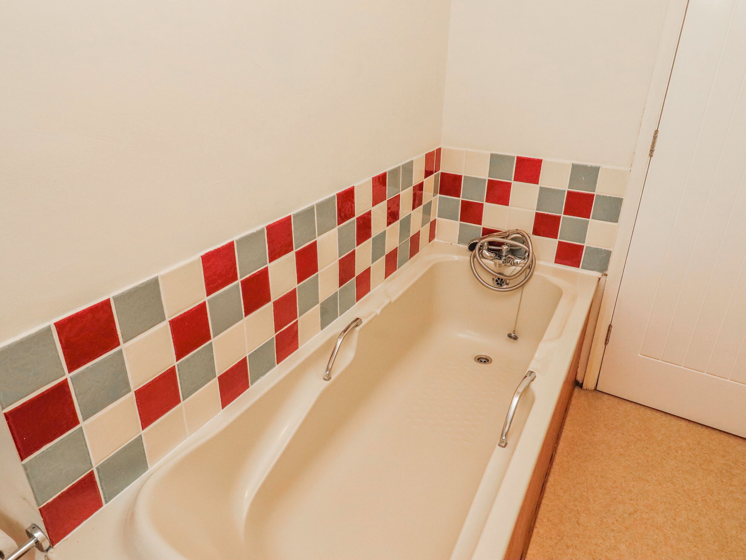 Una vasca da bagno con bordo in piastrelle a scacchi, una doccetta e uno scarico.