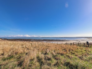A coastal landscape with a clear sky, grassy terrain, and a sandy beach. - St Marys Cottages No4 (Alnwick)
