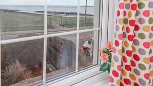 Une fenêtre donnant sur un paysage côtier, un véhicule garé et un rideau à pois.