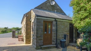 A stone building with a triangular roof, a wooden door, and a satellite dish. - Mossyford Cottage (Alnwick)