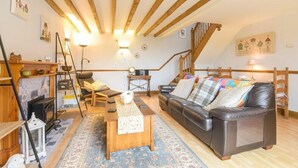 A cozy living room with a fireplace, a sofa, a coffee table, and a staircase leading to an upper level. - Mossyford Cottage (Alnwick)