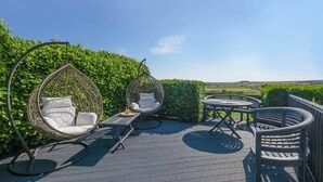 A deck with two wicker chairs, a small table, and a round table with chairs. - Mossyford Cottage (Alnwick)