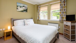A bedroom with a bed, bedside lamp, TV, and storage unit. - The Apartment (Bamburgh)