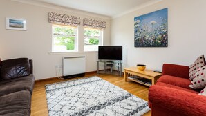 A living room with a brown leather sofa, a red sofa, a glass TV stand, and a painting on the wall. - The Apartment (Bamburgh)
