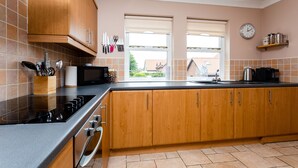 A modern kitchen with wooden cabinets, a black stove, and a window with a view. - The Apartment (Bamburgh)