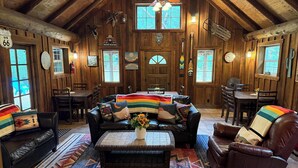 A rustic cabin interior with a high ceiling, wooden walls, and a cozy seating area with a couch and chairs.