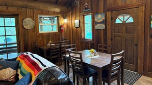 A cozy cabin interior with a wooden dining table, chairs, and a couch with a colorful blanket.
