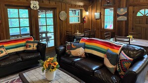 A rustic cabin interior with leather sofas, a dining table, and a large window.
