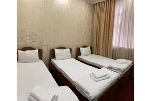 Three single beds with wooden headboards and white bedding, set against a patterned and plain wall.