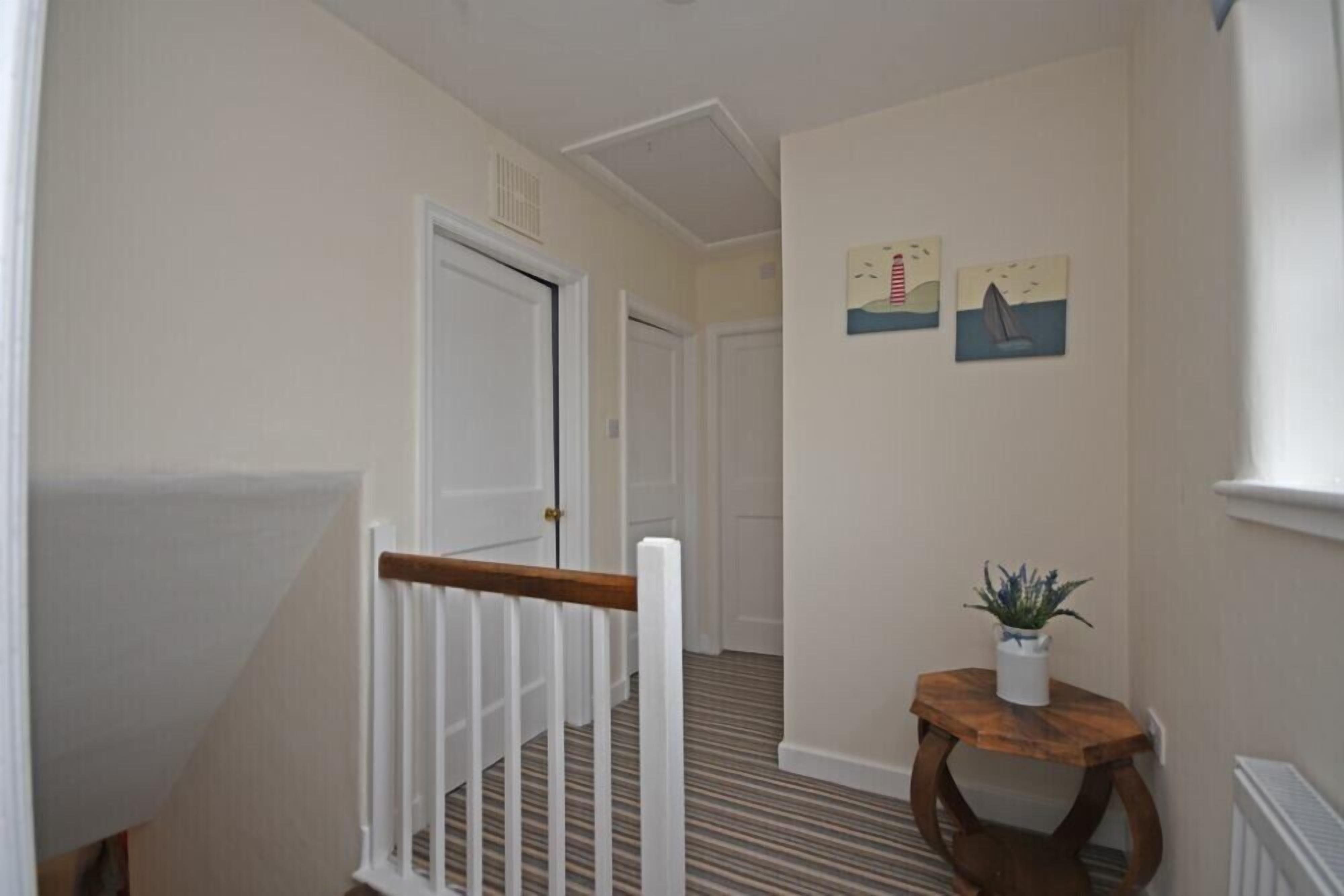 A hallway with a white door, a wooden railing, and a small table with a plant.
