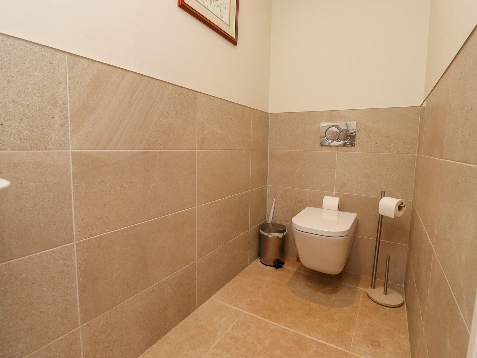 Een kleine betegelde badkamer met een toilet, een prullenbak en een toiletrolhouder.