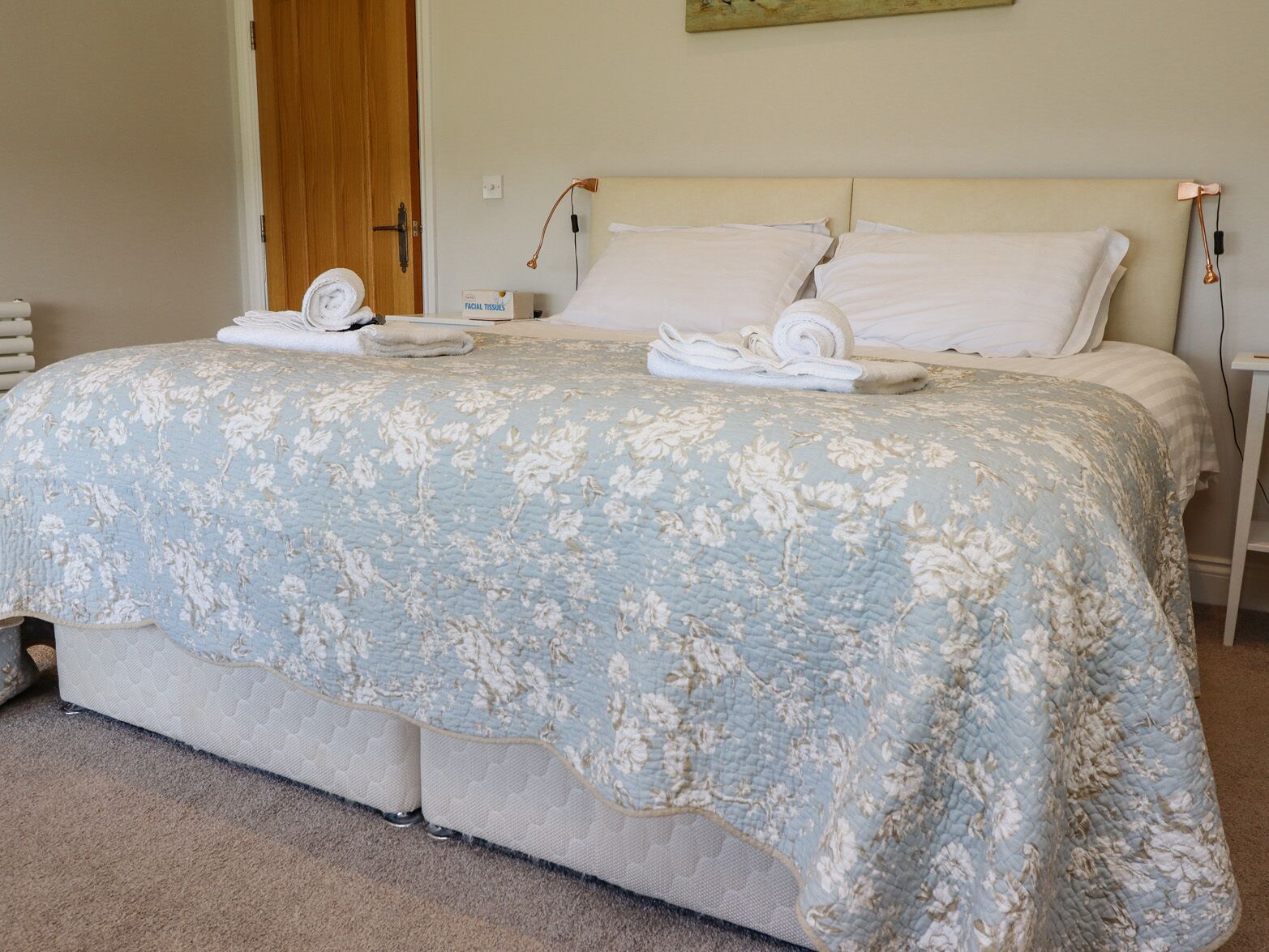 A neatly made bed with a floral-patterned duvet, a bedside lamp, and a box of facial tissues on the nightstand.