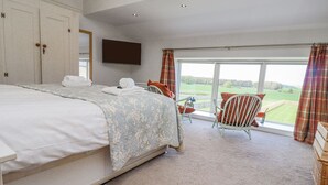 A bedroom with a large bed, a flat-screen TV, a window with curtains, and a view of a green landscape. - The Mustard Pot (Morpeth)