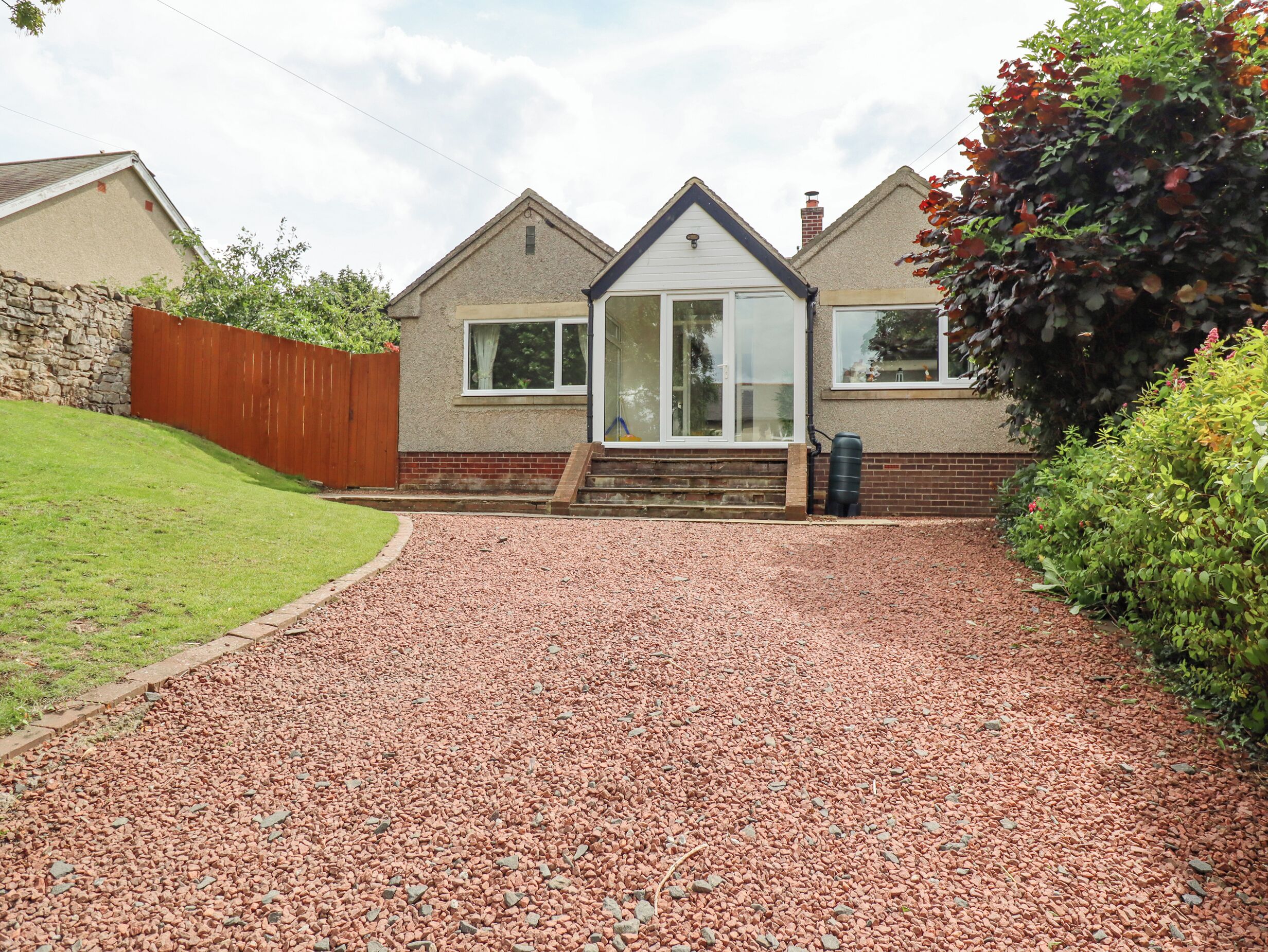 A house with a gravel driveway, a wooden fence, and a brick wall.