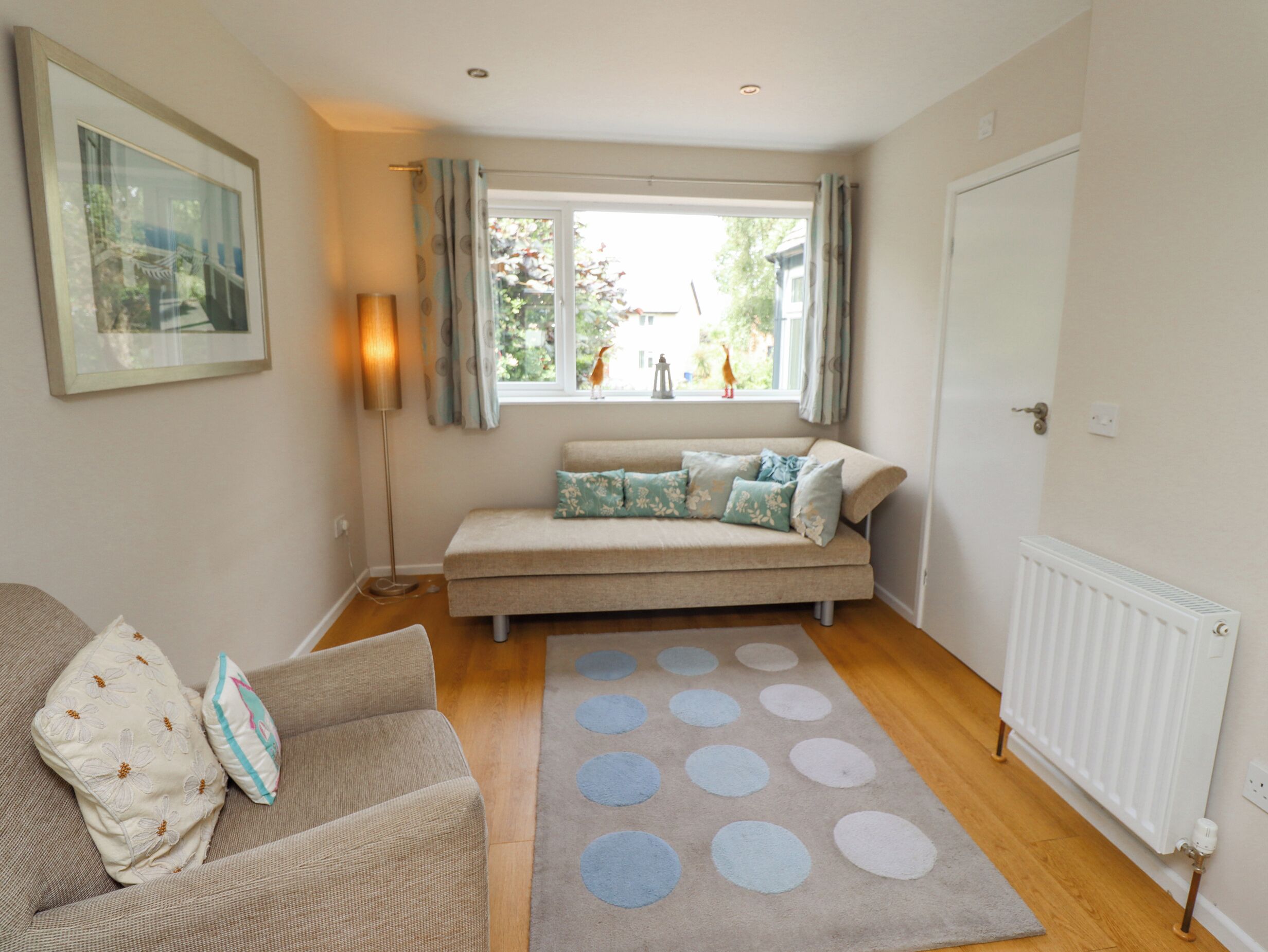 A cozy living room with a sofa, a window with curtains, a floor lamp, and a radiator.
