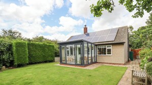 A house with a solar panel roof, a glass conservatory, and a well-maintained lawn. - Manor Cottage (Alnwick)