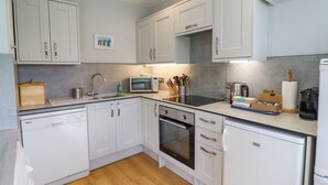 A modern kitchen with white cabinets, stainless steel appliances, and a wooden floor. - Manor Cottage (Alnwick)