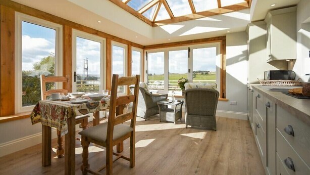 Una habitación amplia con techo alto y ventanas grandes, muebles de madera y vistas al exterior.