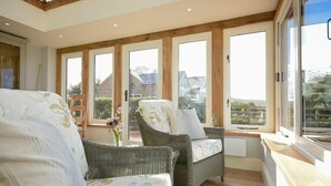 Una habitación luminosa con muebles de mimbre, ventanas amplias y vistas al exterior.