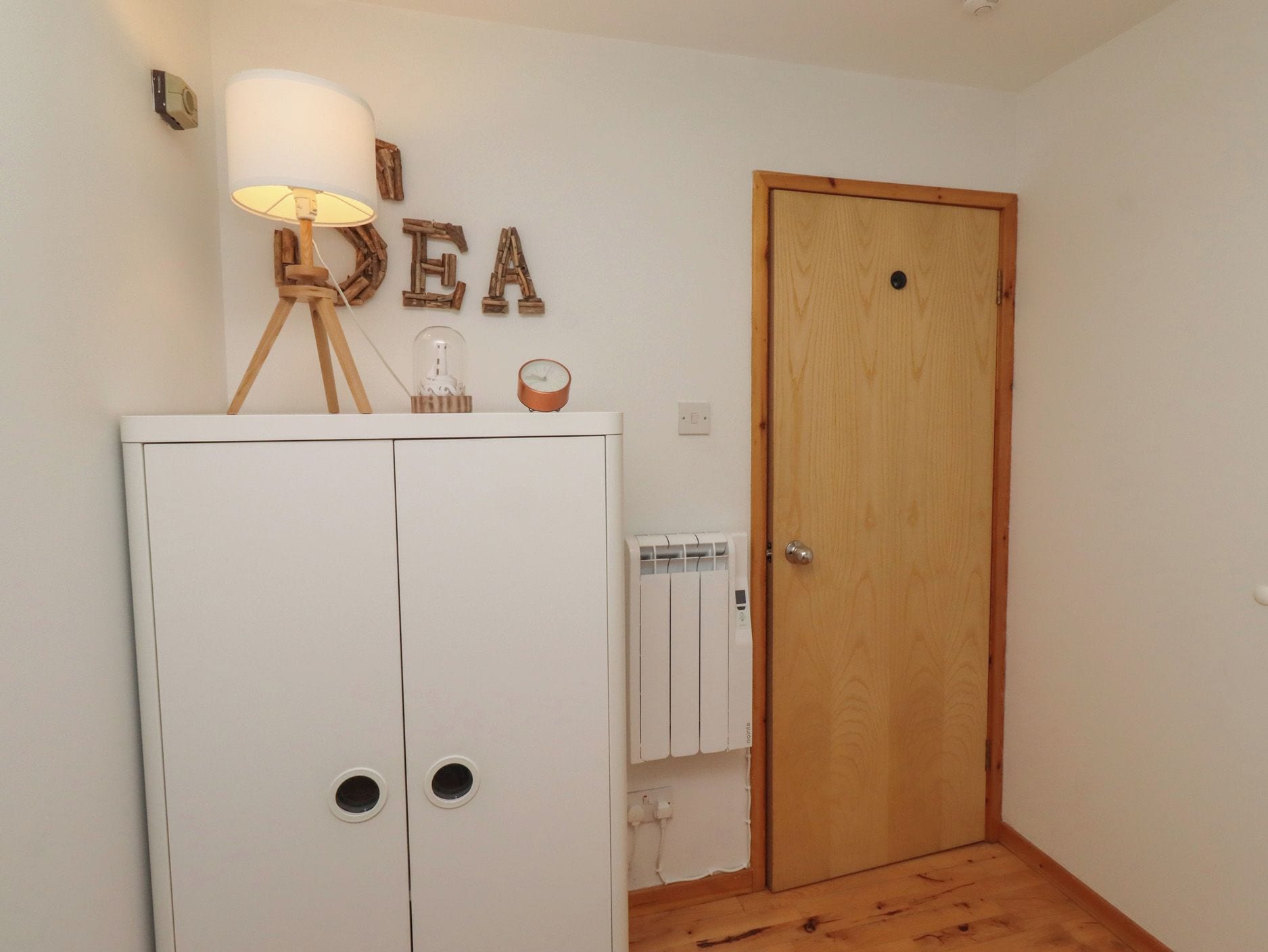 Una habitación con un armario blanco, una puerta de madera, un radiador y una lámpara fijada a la pared.