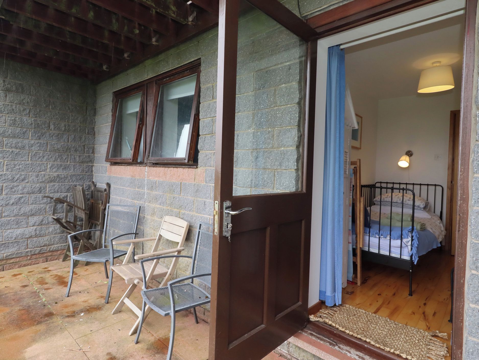 A room with a bed, a window, and a door leading to an outdoor area with chairs.
