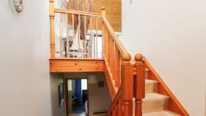 A wooden staircase with a carpeted landing and a view into a room with a blue curtain.
