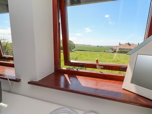 A room with a window overlooking a green landscape and a house. - Links View (Alnwick)