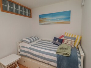 A bedroom with a bed, pillows, a small table, and a painting on the wall.