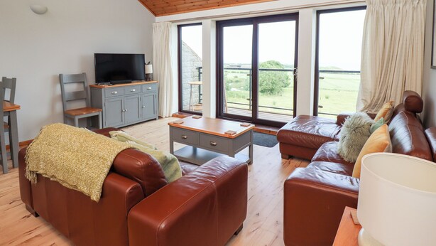 A living room with a wooden ceiling, a television on a cabinet, a sofa, a coffee table, and a large window with a view of the outdoors.