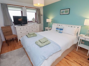 Un dormitorio con cama, televisor, una silla y mesita de noche.