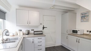 A modern kitchen with white cabinets, a stainless steel sink, a toaster, a kettle, and a microwave. - Whitestacks (Bamburgh)