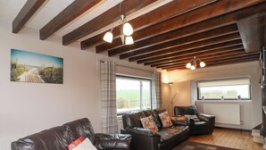 A cozy living room with leather sofas, a wooden floor, and a view of the outdoors through large windows. - Whitestacks (Bamburgh)