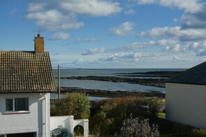 Une maison située sur la côte, avec un toit en tuiles, des murs blancs et une vue sur la mer et le rivage rocheux.