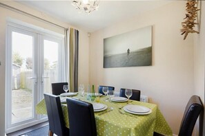 Un coin repas avec une table dressée pour quatre personnes, des chaises et un tableau accroché au mur.