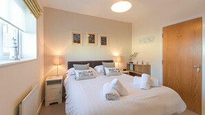 A neatly arranged hotel room with a large bed, bedside lamps, a wooden door, and framed pictures on the wall. - Coast View (Chathill)