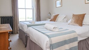 A hotel room with two beds, a window with curtains, a radiator, a bedside table with a lamp, and a framed picture on the wall. - The Lookout (Alnwick)