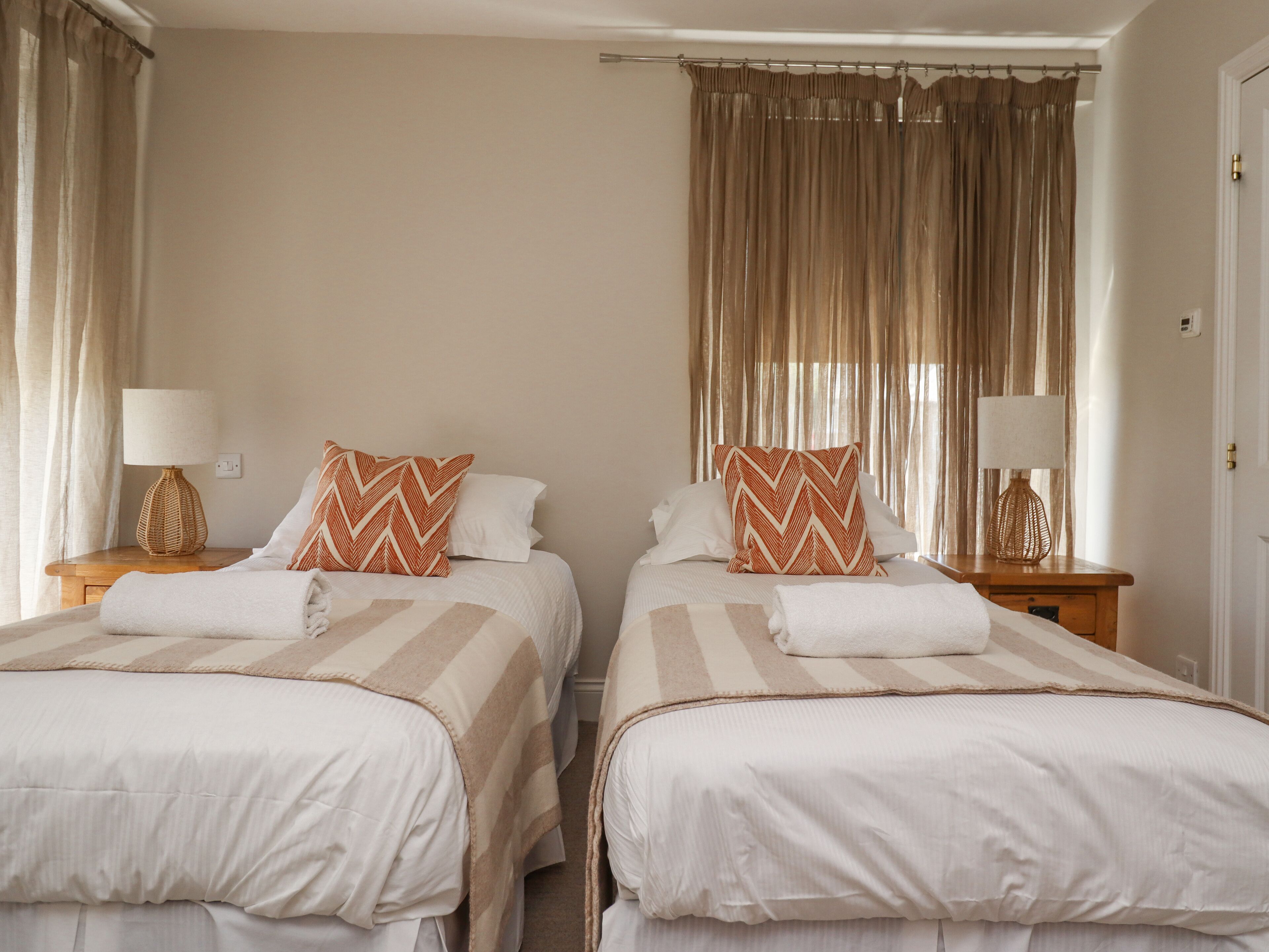 Habitación de hotel con dos camas, paredes color beige y cortinas.