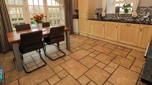 A kitchen with a dining table, chairs, and a view of the outdoors through large windows. - Lapwing Cottage (Bamburgh)