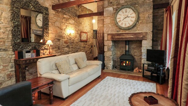A cozy living room with a stone wall, a white sofa, a fireplace, and a clock. - Lapwing Cottage (Bamburgh)
