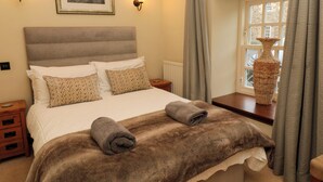 A neatly made bed with a fluffy blanket and two rolled towels, a framed picture on the wall, and a vase on the nightstand. - Lapwing Cottage (Bamburgh)