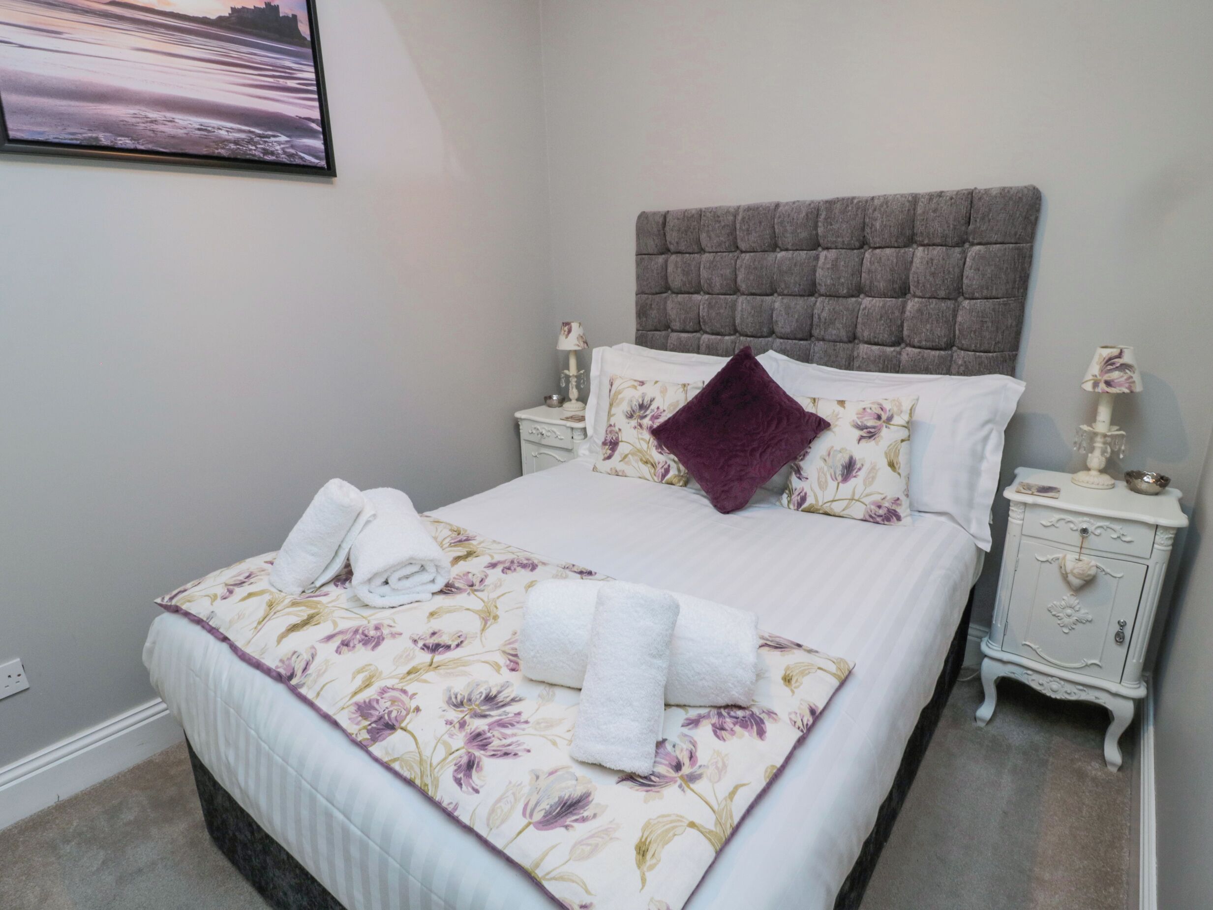 A neatly made bed with floral bedding and a headboard, two bedside tables with lamps, and a framed picture on the wall.