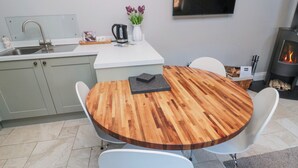 A modern kitchen with a wooden dining table, white chairs, a built-in sink, and a flat-screen TV. - Nurse's Cottage (Alnwick)