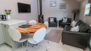 A modern living space with a wooden dining table, white chairs, a black leather sofa, and a fireplace. - Nurse's Cottage (Alnwick)