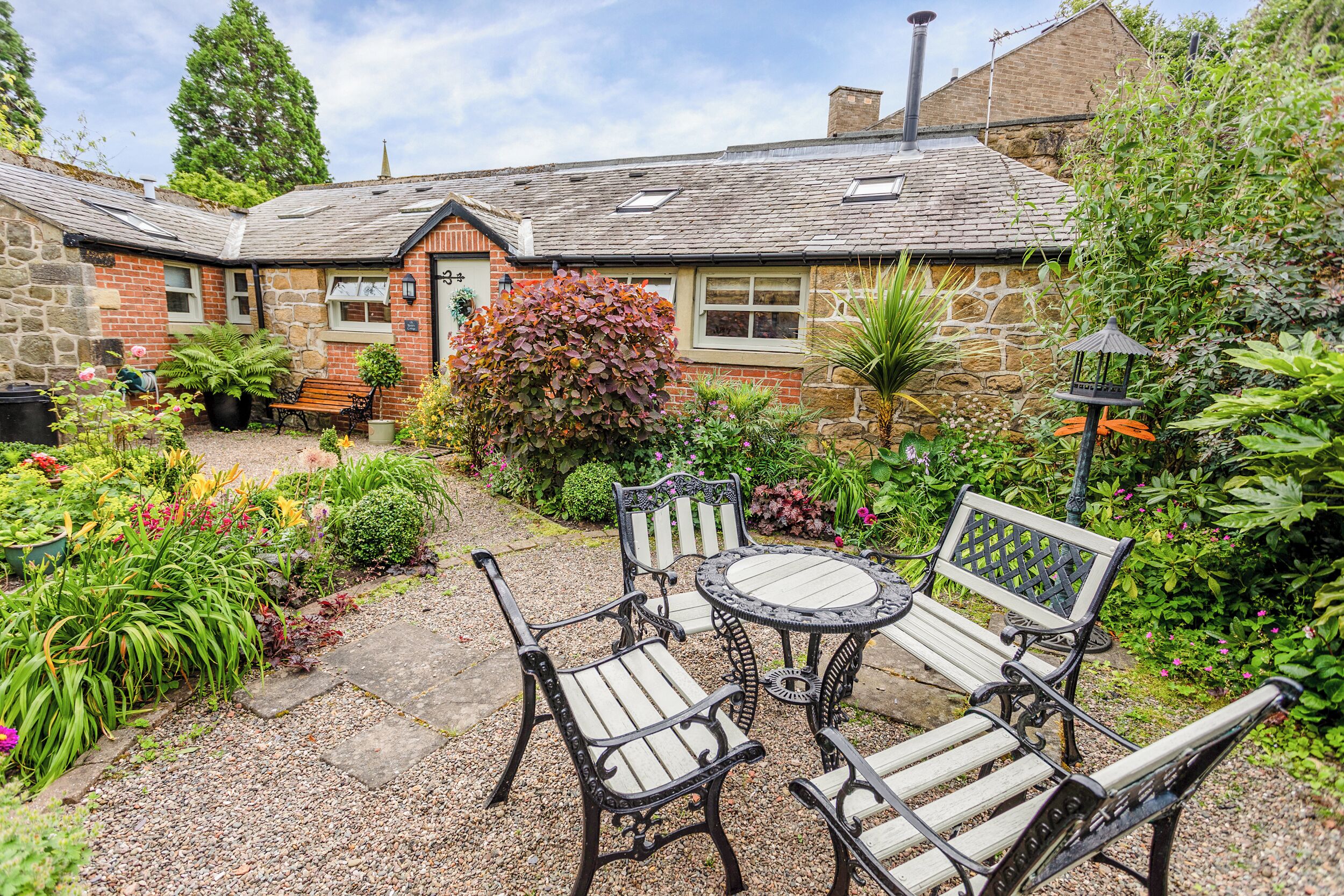 A stone building with a garden patio featuring wicker furniture and a variety of plants.