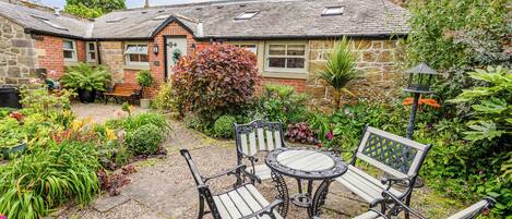 A stone building with a garden patio featuring wicker furniture and a variety of plants.