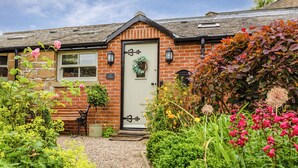 A brick house with a white door, a bench, and a gravel path leading to the entrance. - Nurse's Cottage (Alnwick)