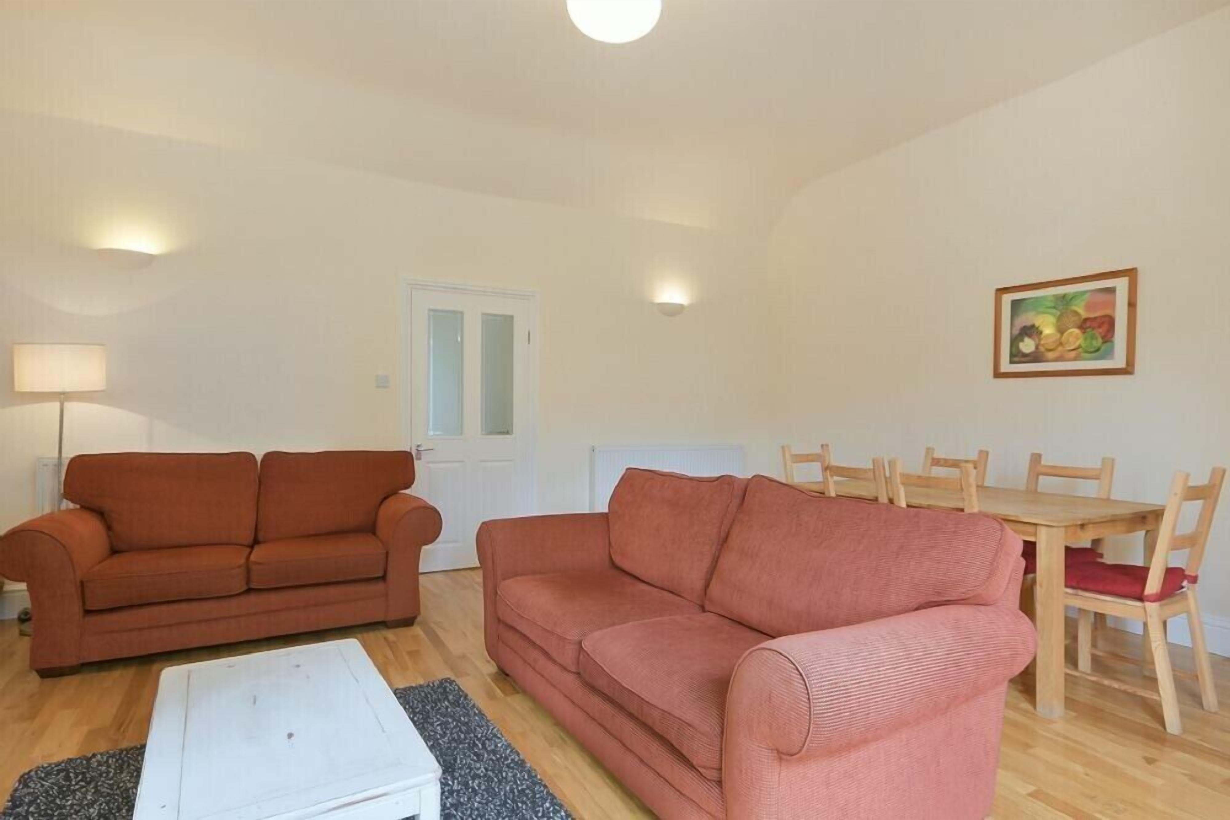 A living room with two sofas, a coffee table, a dining table with chairs, and a painting on the wall.